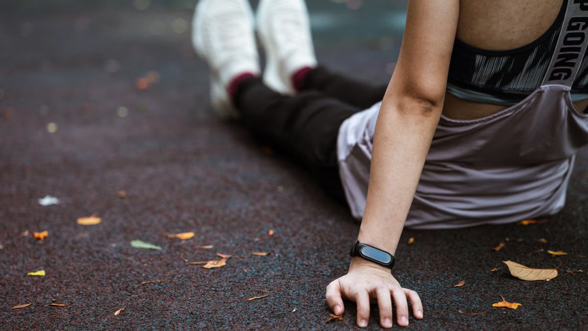 Back view of anonymous female in sportswear and smart watch resting after exercising on sports ground