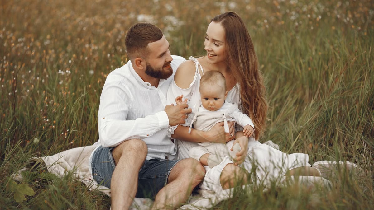 A joyful couple with their baby sitting on a blanket in a sunny meadow, embracing the beauty of summer.